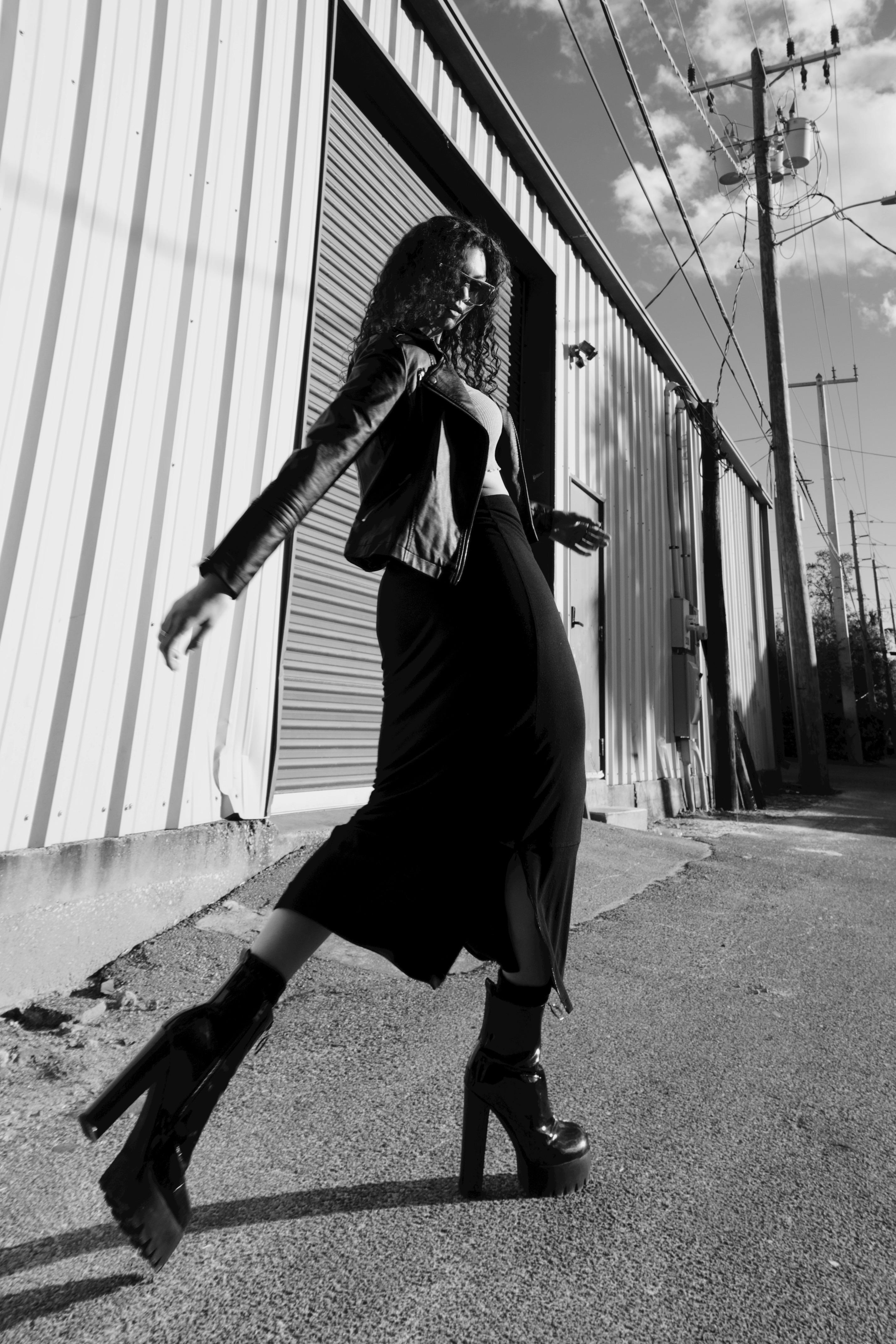 A black-and-white editorial image of a woman moving through an industrial city edge.